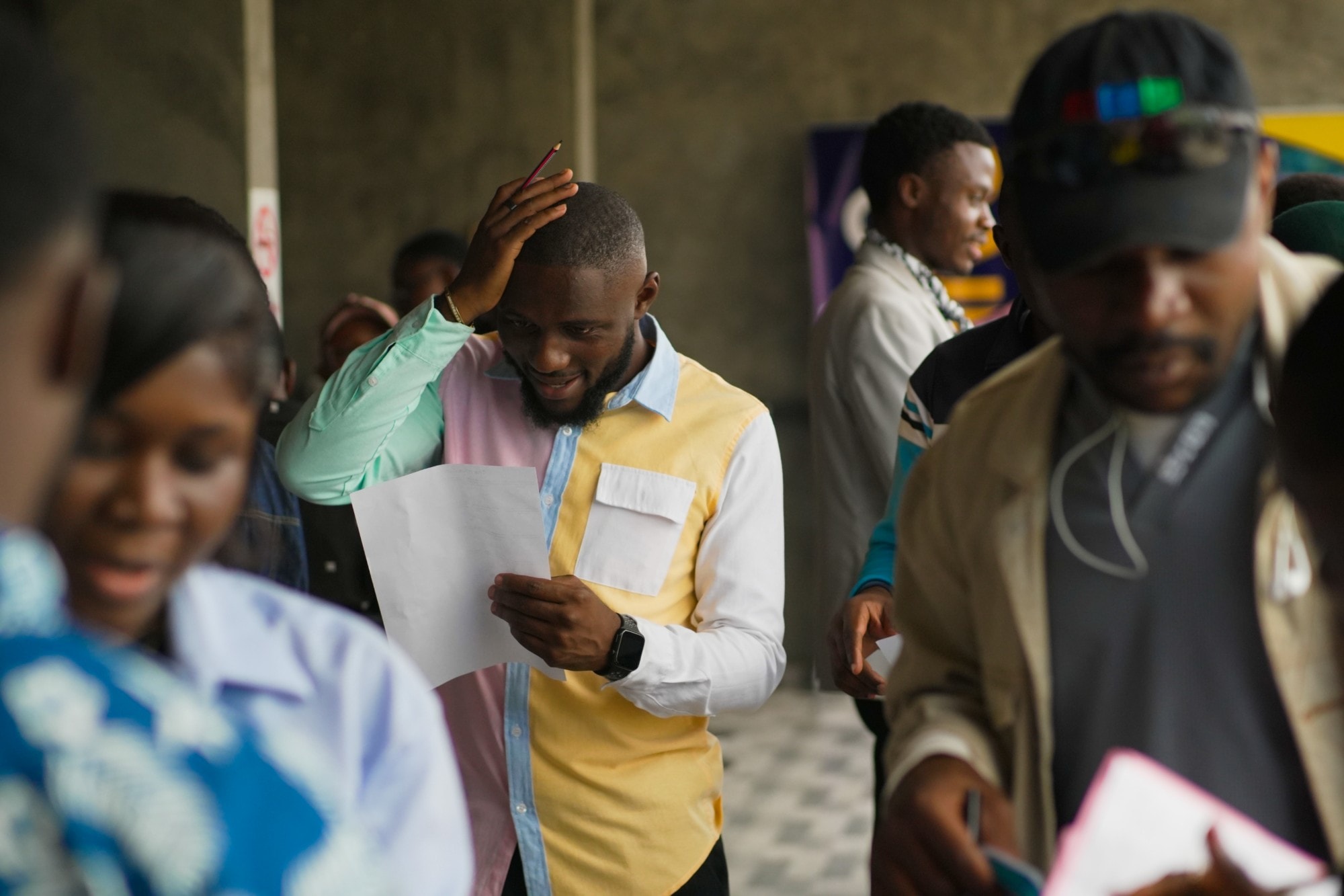 A young man reads a sheet of paper with his hand on his head in a busy queue at a career event